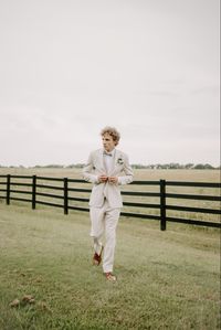 Groom is wearing mens wear house suit in tan, with sage green bow tie and brown shoes.