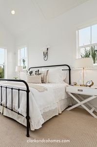 Soft, white and sun-soaked, this guest bedroom has a brilliant white color scheme contrasted by the black wrought iron bed frame. Eyelet linen bedding, soft and feminine, is grounded by woven bisque-colored berber carpeting. #guestbedroom #modernfarmhouse