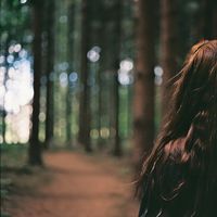 An aesthetic photograph a female model with brunette hair standing in a forest.