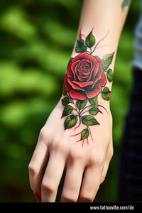 Ein fesselndes Tattoo auf einer Hand ist eine üppige rote Rose, umgeben von detaillierten grünen Blättern. Die leuchtenden Farben des Tattoos kontrastieren wunderschön mit der Haut der Trägerin, während ihre Finger mit passendem rotem Nagellack geschmückt sind.