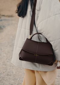 The "Mokki" model showcases the art of folding with its textured leather. The corners are cut to reveal smooth leather for a subtle interplay of textures. The bag’s interior is roomy and divided into compartments, all protected by a flap that features an engraved clasp. With its adjustable shoulder strap held in place by snap hooks, the model smoothly adapts to your movements.