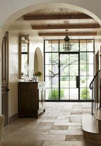 Steel door, bleached wood ceiling, limestone floor, plaster walls, arched doorways