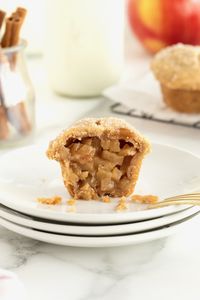 A two-bite apple pie cut in half on a stack of small white plates.