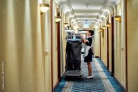 Stock Image: Quality cleaning. Full-length shot of hotel maid in uniform standing in front of chambermaid trolley. Room service concept.