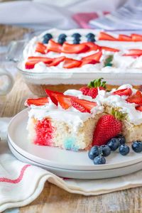 An easy 4th of July poke cake recipe made with jello and topped with cool whip and an American flag made of fresh strawberries and blueberries. #4thofjulydessert #patrioticdessert