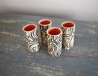 A set of 4 hand sculpted ceramic shot glasses with a hand painted black and white groovy line design and a cheeky pink interior.