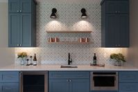 Blue cabinets in a modern wet bar. Brushed stainless appliances. Geometric tile backsplash. Black fixtures. Black sconce lights. Under mount lighting.