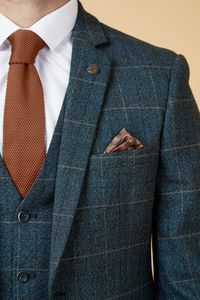 Show up in style with the blue Scott three piece suit. This vintage inspired suit draws inspiration from old age country tweeds, featuring a subtle check laid upon a durable heavyweight fabric, making it ideal for imitating that suave Peaky Blinders style. Character is added with the navy velvet contrast pocket trims and an eye-catching orange paisley pocket square peeking through the top pocket. Model wears size 40R blazer, 40R waistcoat & 34R trousers. Features Slim fit Single-breasted Notch l