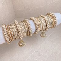 Large stack of luxurious Heavy Pearl & Antique Gold bangles with cream and pale gold shades finished with jhumka drops and Clear stonework. The perfect stack for any Bride or those wanting to make a statement. Ready to Ship as pictured.