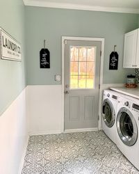 Gray door is fitted into a light green wall with white beadboard wainscoting. A white washer and dryer are placed next to the door in this laundry room featuring white and gray mosaic flooring.