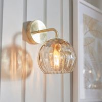 The Dimple Wall Light boasts a modern classic design style with a striking satin brass plated finish. Complete with a luxurious champagne lustre dimpled glass shade, this light fixture adds a touch of elegance and sophistication to any space. Illuminate your home with this timeless piece.