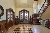 This foyer features arched french doors with carved wood candles on its sides. It includes a wooden staircase illuminated by a pendant light.