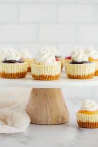 These Mini Cheesecakes feature a homemade graham cracker crust with a smooth and creamy cheesecake filling. This recipe is incredibly easy to make and includes several different topping options to use too! #minicheesecakes #mini #cheesecake #homemade #livewellbakeoften