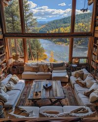 A bright living room with large windows showcasing a beautiful river and surrounding autumn landscape.