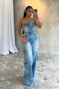 Washed denim tube jumpsuit featuring cross patch design and pocket details Baggy wide leg fit Fly button and zipper closure with an elastic waistband We recommend wearing pasties, a strapless bra, or no bra with this garment Runs true to size