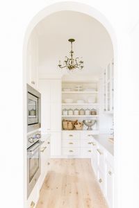 Our white butler's pantry reveal with an arched doorway, vintage chandelier lighting and open shelving.