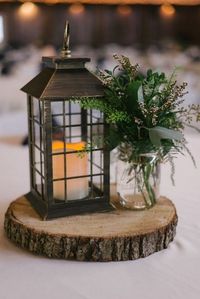 black lantern, greenery and tree stump wedding centerpiece