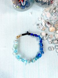 A beautiful hand-beaded bracelet with natural semiprecious larimar gemstone, glass and crystal beads in a blue ombré color scheme.