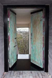 Main Entrance | Vintage door repurposed as the main door of the house, black metal frame, concrete columns and volcanic rock flooring with pebble detail. Forest view, black granite floor. | Mexico City #HuacalEstudio #InteriorDesign #Mexico #MadeInMexico #Styling #Decor #MainEntrance