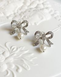 Abella Bow Earrings, these silver earrings feature a delicate bow design adorned with a lustrous shell pearl. Perfect for adding a playful touch to any outfit.