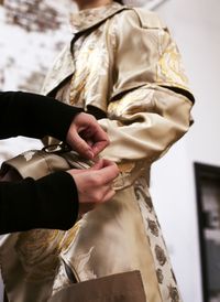 An oversized cotton gabardine trench coat with panels of contrasting duchesse silk roses and garden blooms is fitted in the atelier. From the Alexander McQueen Spring/Summer 2018 pre-collection.