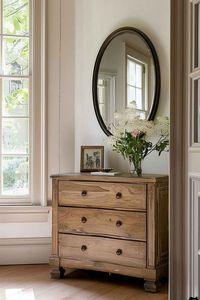 Add a touch of vintage charm to your home with this beautifully styled wooden dresser. Paired with a simple oval mirror and a delicate floral arrangement, this decor setup is perfect for creating a cozy and inviting atmosphere in any room. #VintageDecor #WoodenFurniture #HomeStyling #RusticCharm #InteriorDesignIdeas