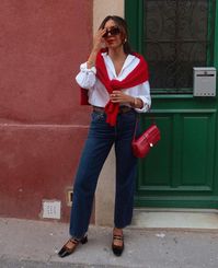 This outfit combines a white button-down shirt, blue jeans, and a red sweater draped over the shoulders, creating a timeless and casual look perfect for a business casual fall wardrobe. The classic pieces and pop of color make this ensemble both stylish and comfortable.   Photo credit by: @lesperlesdebrunette