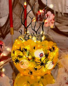 a glass vase filled with yellow lights and spider decorations on top of a table next to candles