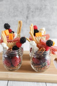 two mason jars filled with fruit, cheese and crackers on top of a wooden cutting board