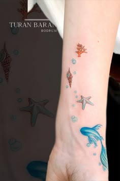 a woman's hand with an ocean themed tattoo on her left wrist and starfish, corals, and seaweed