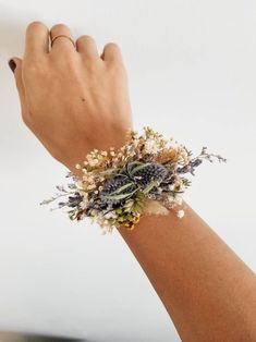 a woman's hand with a bracelet made out of dried flowers and leaves on it