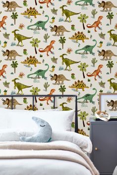 a child's bedroom with dinosaur wallpaper and white bedding in front of the headboard