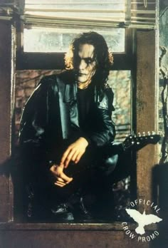 a man with long hair and makeup sitting in a window sill holding an electric guitar