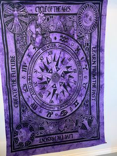 a purple and black tapestry hanging on the wall in front of a white wall with an image of a circle of the ages