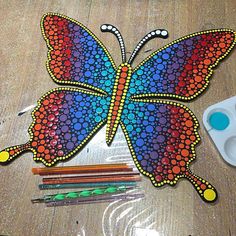 a colorful butterfly is sitting on the table next to colored pencils