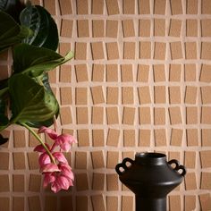 a black vase sitting on top of a table next to a wall with a plant in it