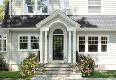 a white house with flowers in the front yard and steps leading up to it's entrance