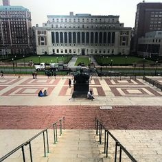 some people are sitting on the steps in front of a large building with many windows