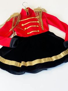 a red and black dress with gold trims on the skirt is sitting on a white surface