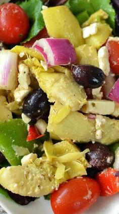 a salad with chicken, olives, tomatoes and lettuce on a white plate