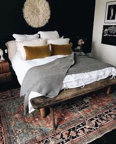 a bed with pillows and blankets on top of it next to a wooden bench in front of a black wall