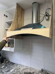 a man is working on a stove hood in a kitchen with white tile and wood