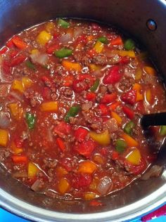 a pot filled with stew and vegetables on top of a blue table cloth next to a wooden spoon