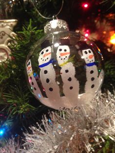 a christmas ornament with three snowmen hanging from it's side on a tree