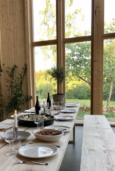 a long table with plates and wine glasses on it in front of large windows that look out onto the countryside