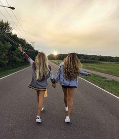 two girls walking down the middle of an empty road with their arms in the air