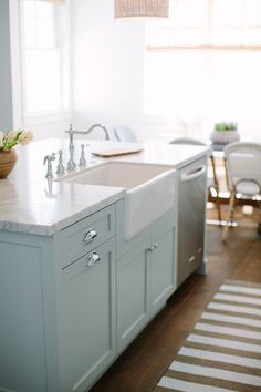 a kitchen with a sink, dishwasher and chairs in the background on a wooden floor