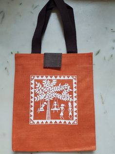 an orange tote bag with white designs on the front and side, hanging from a black strap