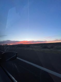 the sun is setting over an open field from a vehicle's windshield, as seen from inside a car