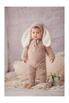 a baby wearing a bunny costume standing on a bed